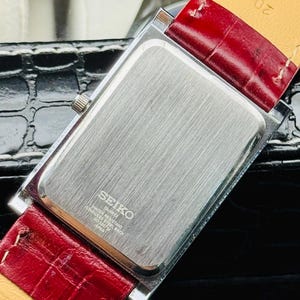 May include: A rectangular Seiko quartz watch with a silver-toned back and a red leather strap. The watch has a silver crown and the back is engraved with "SEIKO QUARTZ WATER RESISTANT STAINLESS STEEL BACK 7N43-0070 JAPAN".