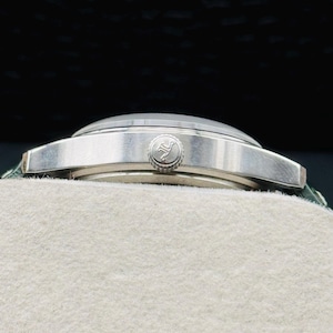 May include: A silver wristwatch with a round face and a textured band. The watch has a silver bezel and a small, circular crown. The watch is resting on a white surface.