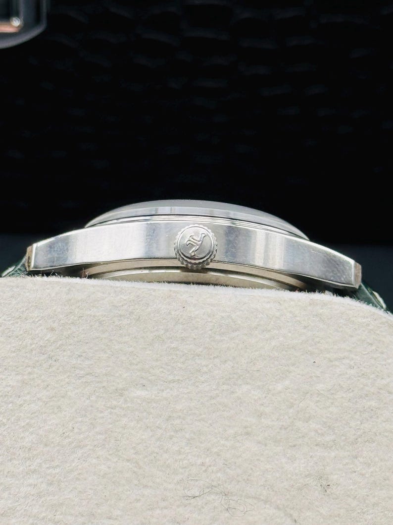 May include: A silver wristwatch with a round face and a textured band. The watch has a silver bezel and a small, circular crown. The watch is resting on a white surface.