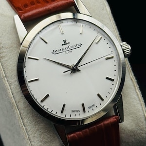 Puede incluir: Un reloj Jaeger-LeCoultre Club plateado con esfera blanca y correa de cuero marr&oacute;n. El reloj presenta agujas e indicadores plateados, y la esfera muestra el logotipo de Jaeger-LeCoultre. La correa es de un color marr&oacute;n rojizo intenso.