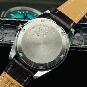 May include: A stainless steel Seiko watch with a brown leather strap. The watch back displays the Seiko logo, model number 335718, and the words "Water Resistant" and "Stainless Steel". The strap is marked "18".