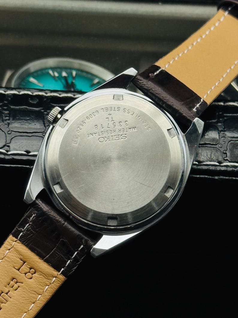 May include: A stainless steel Seiko watch with a brown leather strap. The watch back displays the Seiko logo, model number 335718, and the words "Water Resistant" and "Stainless Steel". The strap is marked "18".