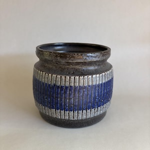 May include: A small, cylindrical ceramic vase with a dark brown rim and base. The body features a band of vertical blue and silver stripes. The vase has a textured surface and a dark interior.