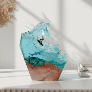 Può includere: Scultura decorativa in resina raffigurante un surfista su un'onda. L'onda è blu traslucido, con un surfista nero. La base è marrone e verde, con vita marina visibile. Oggetto decorativo.