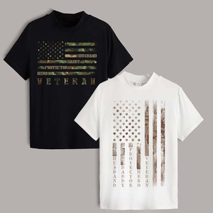 May include: A black t-shirt and a white t-shirt, each featuring a graphic of an American flag. The black shirt has a camouflage flag with the words HUSBAND, DADDY, PROTECTOR, HERO, VETERAN. The white shirt has a distressed flag with the same words.