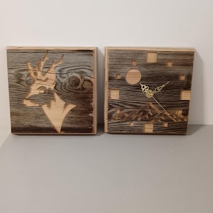 Può includere: Due opere d'arte da parete in legno. Una presenta una testa di cervo intagliata, l'altra un orologio con un paesaggio montano e un quadrante dorato. Il legno ha un aspetto naturale e rustico con tonalità marroni chiare e scure.
