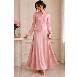 May include: A two-piece set in dusty rose featuring a long-sleeved jacket with a mandarin collar, a front button placket, and buttoned cuffs, paired with a matching floor-length A-line skirt. The fabric has a smooth, satin-like finish.