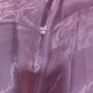 Puede incluir: Primer plano de una tela brillante de color lavanda. El material tiene una calidad transl&uacute;cida, con la luz reflej&aacute;ndose en la superficie, creando reflejos y sombras. La tela parece suave y fluida.