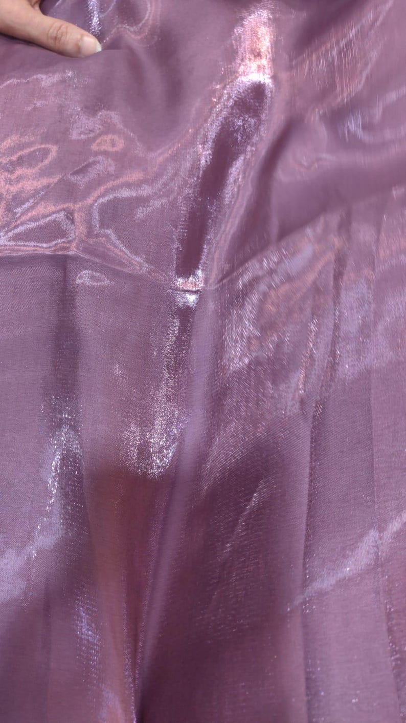 Puede incluir: Primer plano de una tela brillante de color lavanda. El material tiene una calidad transl&uacute;cida, con la luz reflej&aacute;ndose en la superficie, creando reflejos y sombras. La tela parece suave y fluida.
