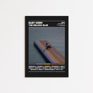 May include: Black framed poster featuring the album art for "The Melodic Blue" by Baby Keem. The poster includes the album title, artist name, and release date. The image shows a person sitting on a colorful dock over water.
