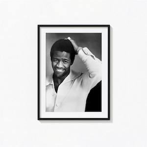 May include: Black and white framed portrait of a smiling person with dark hair, wearing a white collared shirt. The person is touching their hair with one hand, and wearing a ring and bracelet.