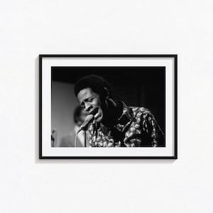 May include: Black and white framed photograph of a man singing into a microphone. The man is wearing a patterned shirt. The image is a medium shot, capturing the singer's face and upper body.