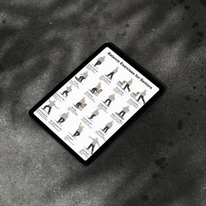 May include: A black tablet displays "Balance Exercises for Seniors" with illustrations of various balance exercises. The exercises include standing on one leg, chair stands, and heel raises. The tablet is angled on a dark gray surface.
