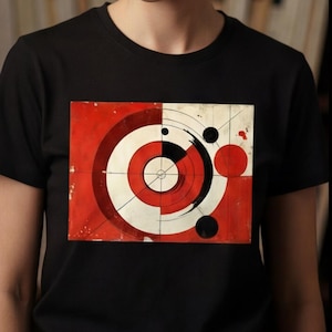 Puede incluir: Camiseta negra con un diseño geométrico en rojo, blanco y negro. El diseño incluye círculos concéntricos y otras formas. La persona de la imagen lleva gafas redondas. El fondo es una estantería.