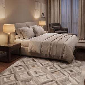 May include: A bedroom scene featuring a bed with light-colored bedding, pillows, and a throw blanket. Two bedside lamps with beige shades sit on dark wood nightstands. A patterned rug in neutral tones covers the floor, and a gray armchair is visible.