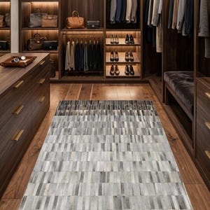 May include: A luxurious walk-in closet with dark wood cabinetry, featuring shelves with handbags, shoes, and hanging clothes. A rectangular rug with a gradient of gray and beige rectangular blocks covers the floor.