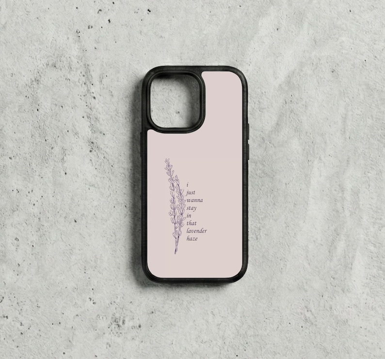 May include: A black phone case featuring a light pink backdrop and a lavender sprig illustration. The text "I just wanna stay in that lavender haze" is printed in dark purple. The case has a black border.