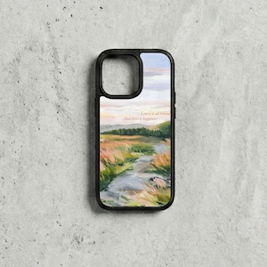 May include: Black phone case with a landscape painting of a river, fields, and trees under a sunset sky. The case has the text "Leave it all behind, And there is happiness."