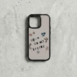 May include: A phone case with a black border and a beige background. The case features the text "this is me trying" in a collage style, with small floral and botanical elements.