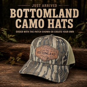 May include: A camouflage baseball cap with a mesh back and a hexagonal leather patch on the front. The patch features the text "BURY ME IN BOTTOMLAND" with a detailed forest graphic. The text "JUST ARRIVED BOTTOMLAND CAMO HATS" is above.