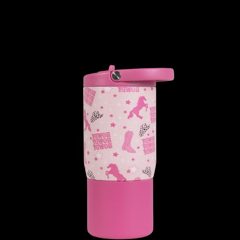 May include: A pink and white tumbler with a cowboy theme. The tumbler features a pink lid and base, with a white center adorned with pink horses, stars, cowboy boots, and the word "HOMDA". The tumbler has a flip-top lid and a handle.