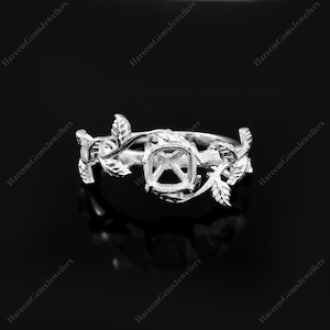 Peut inclure: Une bague argentée dotée d'un anneau orné de feuilles et de vignes sculptées. Le centre de la bague comprend un sertissage à quatre griffes destiné à une pierre précieuse, présentant un motif botanique détaillé entourant le doigt.