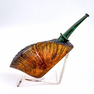 Pode incluir: Um cachimbo de tabaco artesanal com uma tigela de grão de madeira quente e rica e um bocal verde escuro. A tigela tem uma borda texturizada única e é exibida em um suporte de acrílico transparente. O design mostra uma mistura de materiais naturais e artesanato.