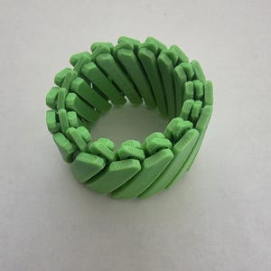 May include: A green bracelet with a repeating geometric design. The bracelet is made of rectangular segments that are connected to form a circular shape. The color is a bright, spring green.