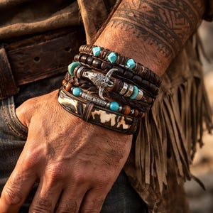 Puede incluir: Conjunto de pulseras apiladas con cuero, cuentas de madera y detalles turquesa. Una pulsera tiene un dije de cabeza de toro plateado, otra tiene una banda estampada.
