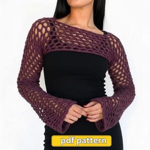 Puede incluir: Un bolero de ganchillo calado de color ciruela con mangas largas. La prenda tiene cuello barco y mangas acampanadas. El texto "pdf pattern" está en un rectángulo amarillo en la parte inferior de la imagen. El bolero se lleva sobre un top negro.