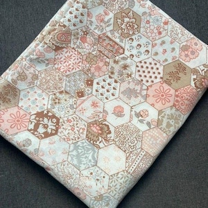 May include: A folded piece of fabric featuring a repeating hexagonal pattern. Each hexagon contains distinct floral, paisley, or geometric motifs in a soft colour palette of muted pink, beige, cream, and light grey tones across the textile surface.