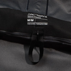 May include: Close-up of a black label from Arc'teryx, with the text "ARC'TERYX MEN'S/HOMMES M/M MADE IN CHINA/FABRIQU&Eacute; EN CHINE". The label is attached to a dark gray garment, with a black loop.