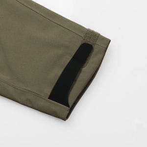 May include: Close-up of a section of olive green fabric with a black accent. The fabric has a textured appearance and is stitched along the edges. A strip of hook-and-loop fastener is visible.