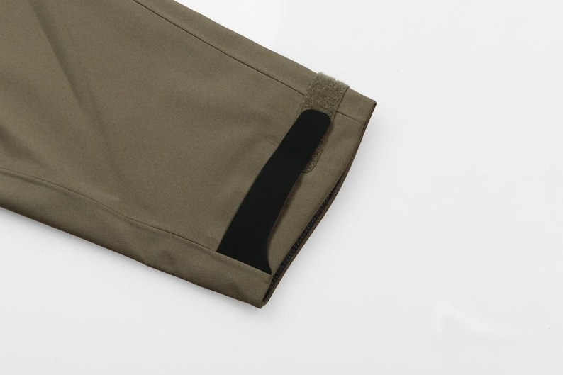 May include: Close-up of a section of olive green fabric with a black accent. The fabric has a textured appearance and is stitched along the edges. A strip of hook-and-loop fastener is visible.