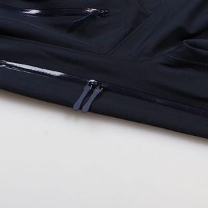 May include: Close-up of a navy blue jacket with a zipper closure. The jacket has a sleek, minimalist design with a smooth, matte finish. The zipper is dark blue and runs horizontally across the chest.