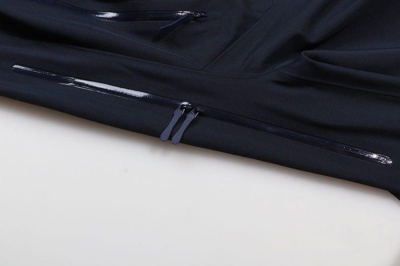 May include: Close-up of a navy blue jacket with a zipper closure. The jacket has a sleek, minimalist design with a smooth, matte finish. The zipper is dark blue and runs horizontally across the chest.
