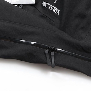May include: Close-up of a black jacket with a prominent zipper and the brand name "ARC'TERYX" in white lettering. The jacket appears to be made of a durable, weather-resistant material, suitable for outdoor activities.