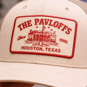 May include: A beige and brown trucker hat with a red rectangular patch. The patch features the text "THE PAVLOFFS" above an illustration of a building, with "Since 2025" and "HOUSTON, TEXAS" below.