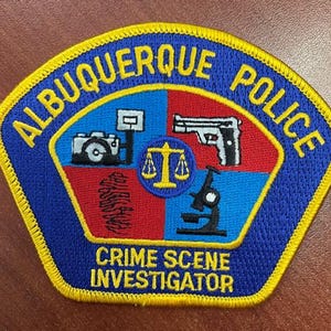 May include: Embroidered Albuquerque Police patch with a blue, red, and yellow design. The patch features a camera, scales, a gun, and a microscope. The text "ALBUQUERQUE POLICE" and "CRIME SCENE INVESTIGATOR" are also included.