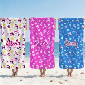 Peut inclure: Trois serviettes de plage rectangulaires avec un motif répétitif de silhouettes, couronnes, cœurs et sacs à main. La serviette blanche porte le nom Alora, la rose le nom Renae et la bleue le nom Yara.