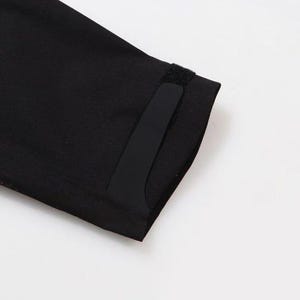 May include: Close-up of a black garment sleeve with a rectangular black patch and a small velcro closure. The sleeve is made of a smooth, dark fabric. The background is plain white.