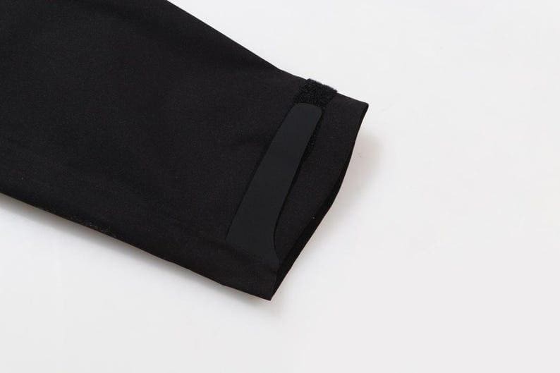 May include: Close-up of a black garment sleeve with a rectangular black patch and a small velcro closure. The sleeve is made of a smooth, dark fabric. The background is plain white.