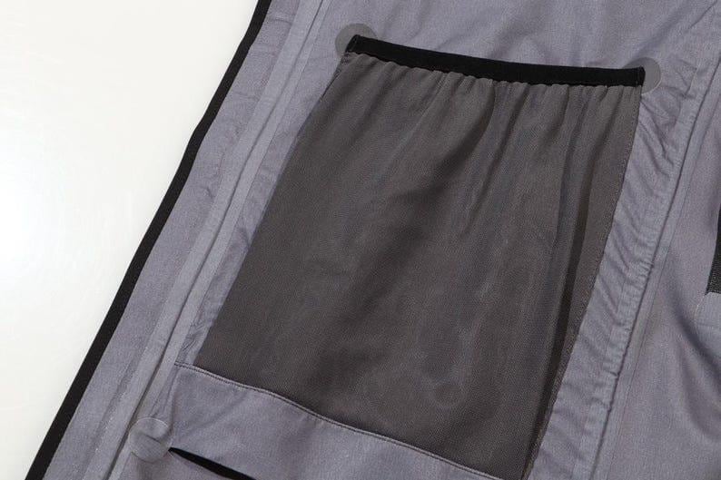 May include: Close-up of a gray garment interior with a large, dark gray mesh pocket. The pocket is outlined with black trim and is sewn into the gray fabric. The garment has a black trim along the edge.