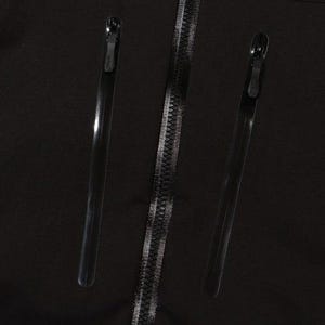 May include: Close-up of a black garment featuring three zippers. Two long, thin zippers flank a central zipper with a silver-colored track. The zippers are all black with silver-colored teeth.