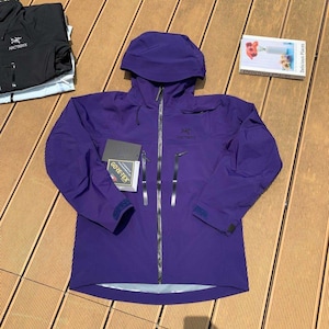 May include: A vibrant purple Arc'teryx Gore-Tex jacket with a hood, zipper closure, and multiple pockets. The jacket has the Arc'teryx logo on the chest and sleeve. A tag with the Gore-Tex logo is attached. Additional black jacket is visible.