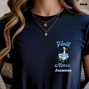 Pode incluir: Camiseta preta com o texto "Float Nurse Jasmine" em script azul claro. A camisa apresenta um ganso de desenho animado usando um gorro de enfermeira e uma boia azul e branca. A palavra "black" é impressa no canto superior direito.