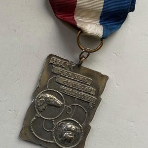 May include: A silver medal with a red, white, and blue ribbon. The medal features the text "The Kennel Club of Philadelphia" and two dog breeds: a Greyhound and a Bulldog.