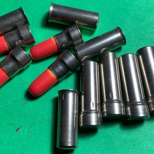 Puede incluir: Un surtido de objetos cilíndricos metálicos con acabado plateado. Algunos tienen una punta roja y redondeada. Los objetos están dispuestos sobre una superficie verde. Parecen ser componentes o piezas.