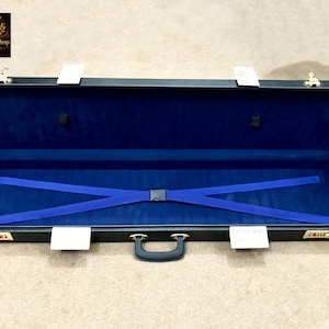 May include: Open black case with a blue interior and blue straps. The case has a black handle and gold-colored latches. The interior is lined with blue fabric. The case is open, revealing the inside.