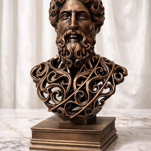 May include: Bronze-colored bust sculpture of a man with a beard and curly hair. The sculpture features intricate, openwork detailing on the chest and is mounted on a square base. The bust is a decorative item.